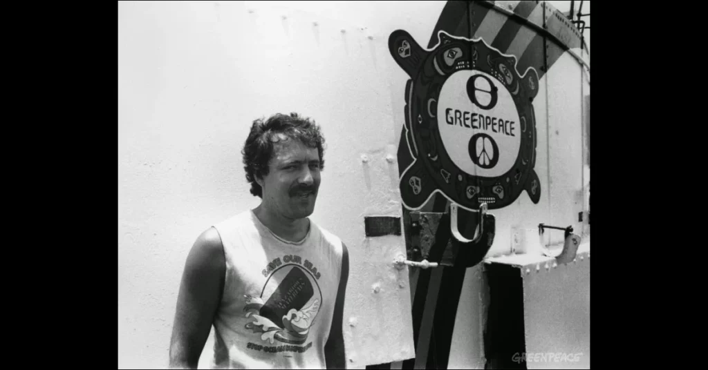 un home recolzat davant un escut de Greenpeace