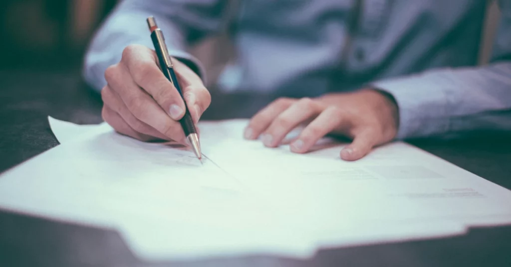 un home escriu uns papers en una taula