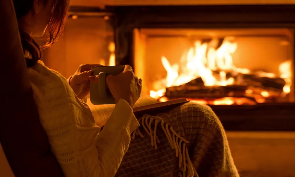 Young woman sitting at home by the fireplace and reading a book.