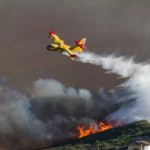 Wild fire close to houses being fought with airplanes and helicopters