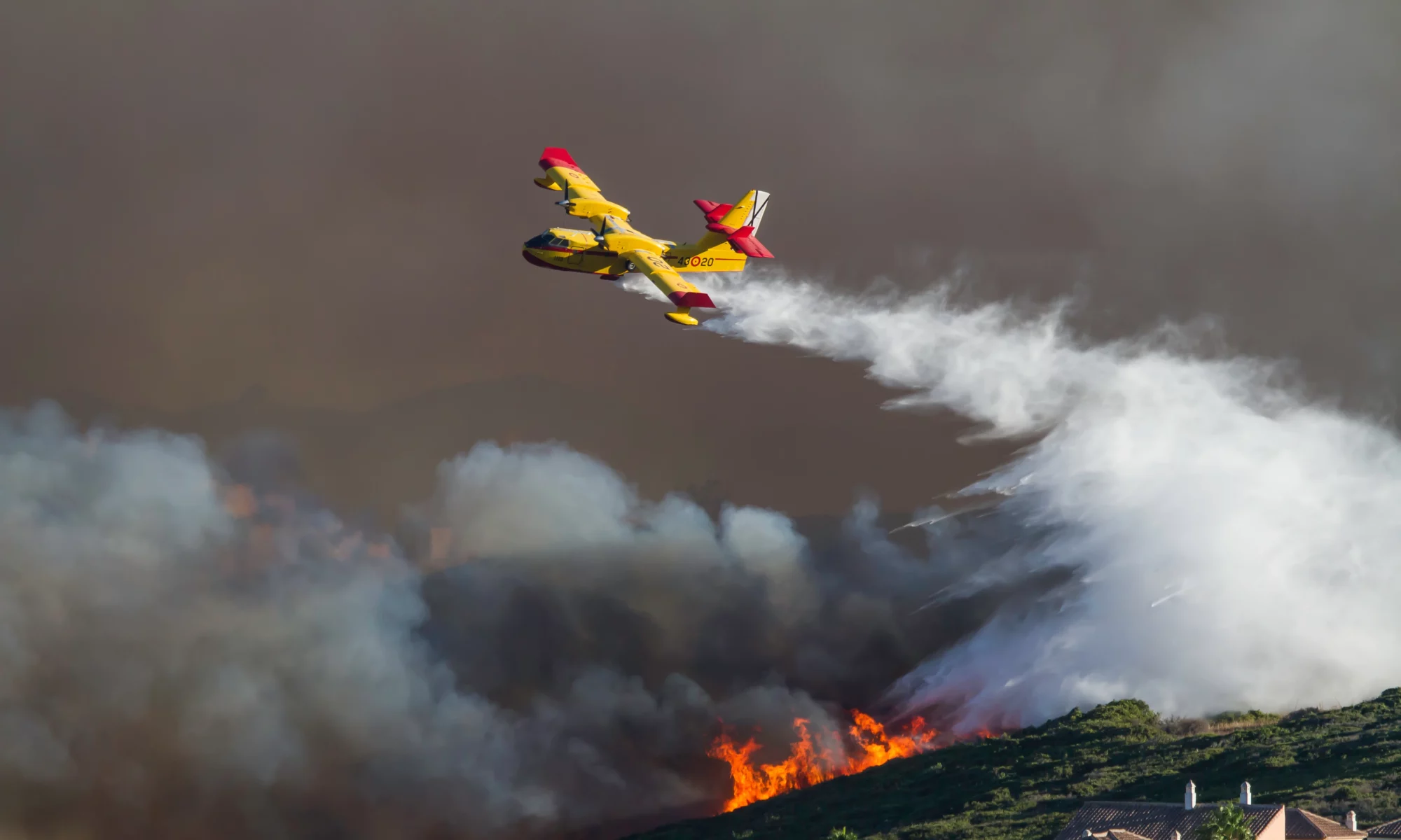 Wild fire close to houses being fought with airplanes and helicopters
