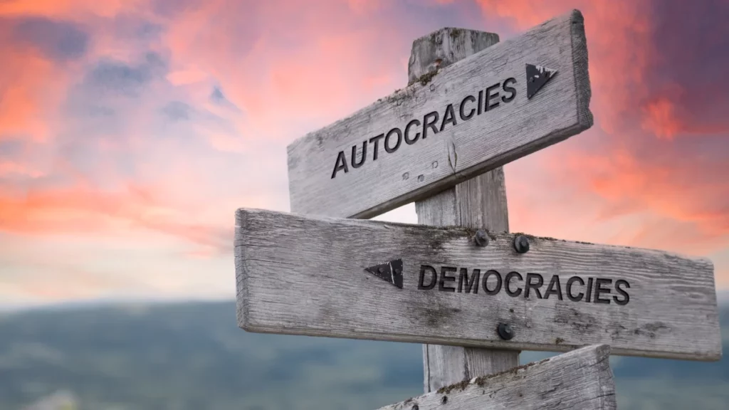 autocracies democracies text quote on wooden sign outdoors in nature. pink dramatic sunset background.