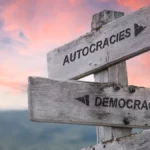 autocracies democracies text quote on wooden sign outdoors in nature. pink dramatic sunset background.