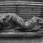 persona dorm en un banc públic