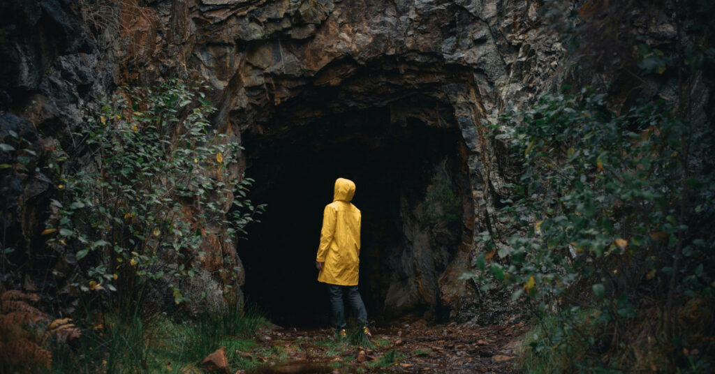 una pesona amb un impermeable groc front l'entrada d'una cova